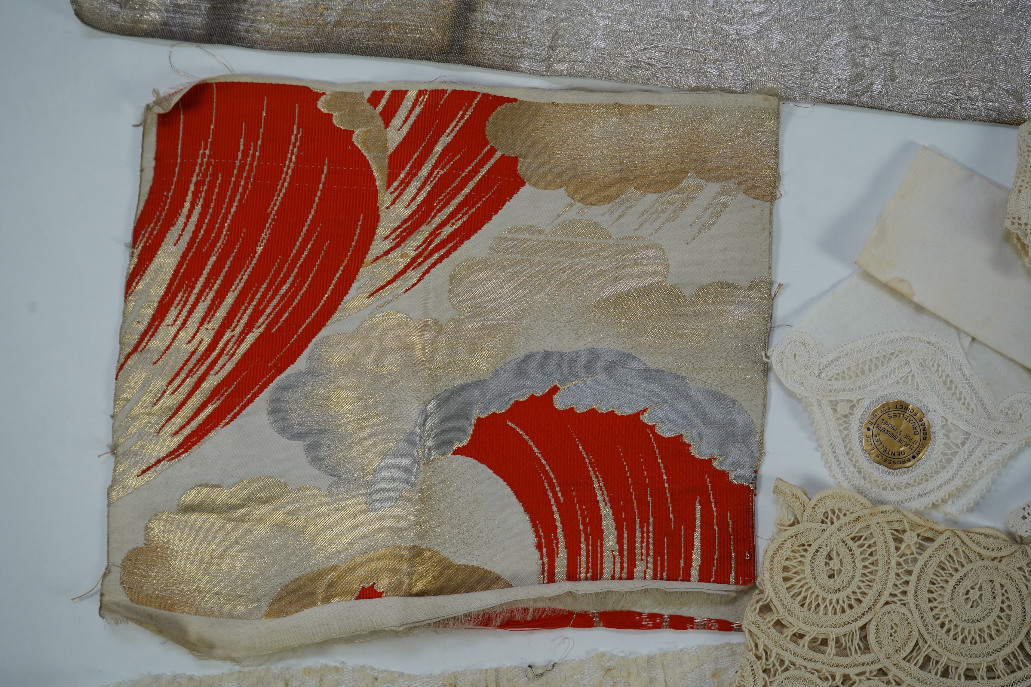 A collection of mixed machine lace: a black lace stole, two black veils, a sample of Japanese brocade, a length of metallic ribboning and various items of cream lace, ribboning 230cm long. Condition - variable poor to fa